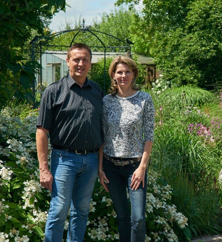 Reiner Winkendick und Dr. Stephanie Winkendick vor üppigen grünen Pflanzen und bunten Blumen.